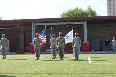 Military members standing at the position of attention in front of flags.